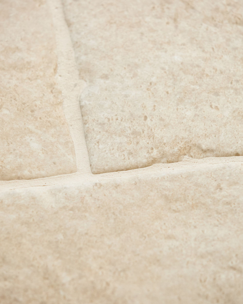 Close-up of Cotswold Porcelain Matt showing the pitted limestone-look surface and softened tumbled edges where three tiles meet