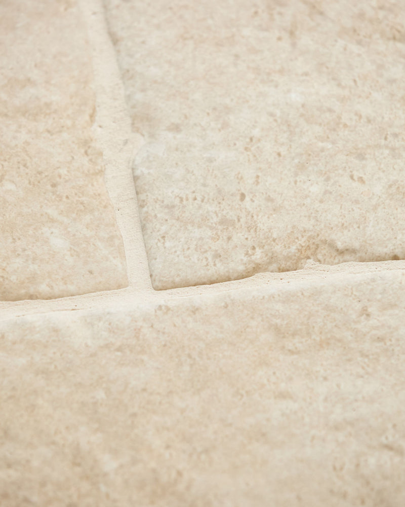 Close-up of Cotswold Porcelain Matt showing the pitted limestone-look surface and softened tumbled edges where three tiles meet