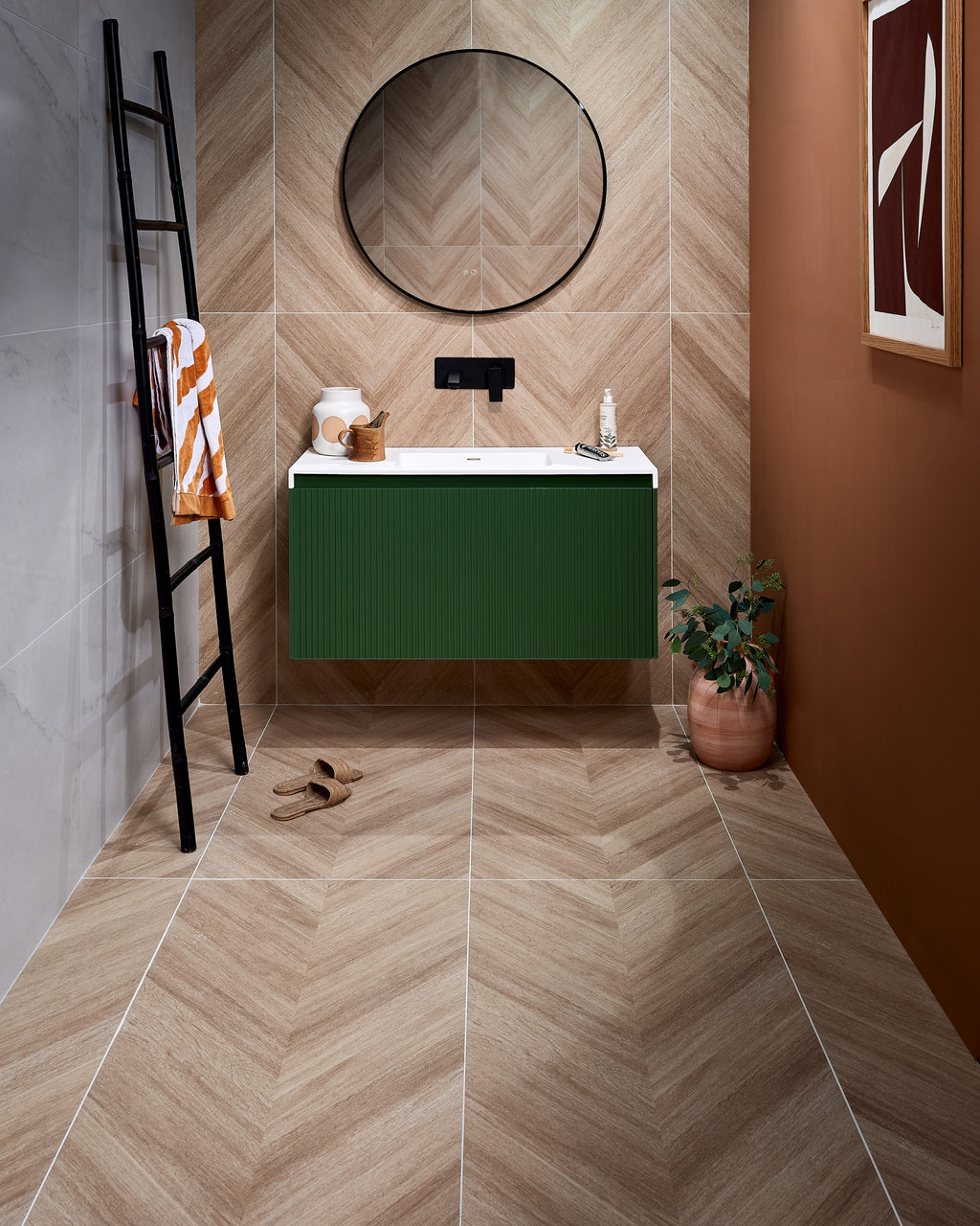 Davos Chevron Porcelain Matt laid in a chevron across the floor and up the wall of a cloakroom, with Mystery White Porcelain Matt on the side wall, a green fluted vanity and a black leaning towel ladder