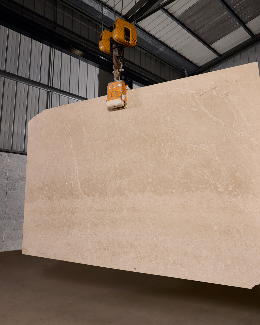 Domus Marble Slab, a full bespoke slab of honed cream marble suspended from an overhead gantry hoist in the stone warehouse