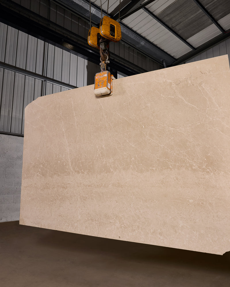 Domus Marble Slab, a full bespoke slab of honed cream marble suspended from an overhead gantry hoist in the stone warehouse