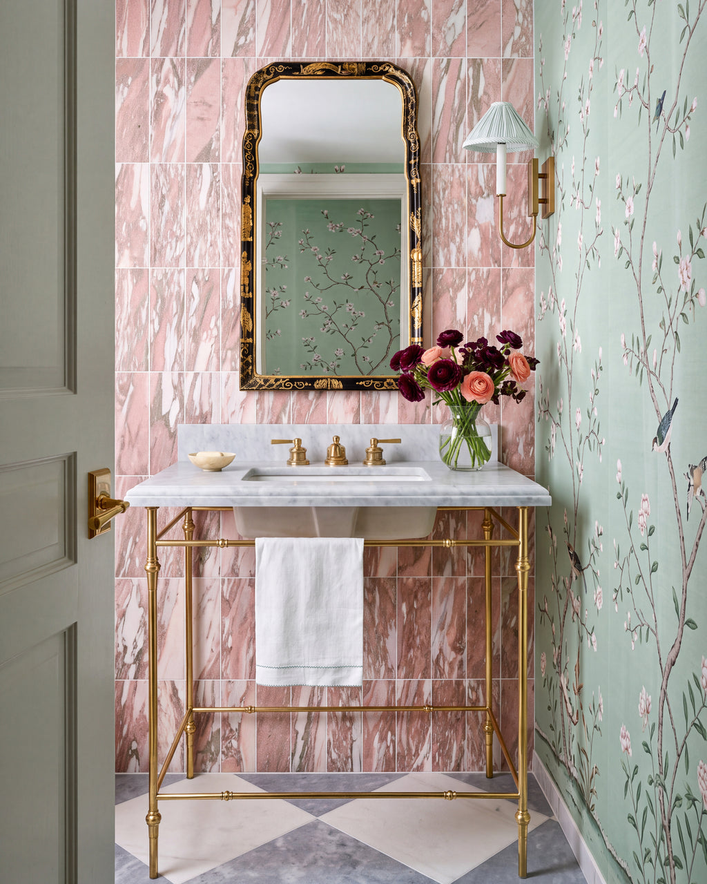East Java Flamingo Marble Honed Brick tiled floor to ceiling in a cloakroom, with a brass washstand and marble top, a gilt chinoiserie mirror, a pleated wall light and green blossom wallpaper on the return wall