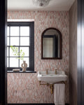 East Java Flamingo Marble Plume Mosaic running floor to ceiling in a small cloakroom with black joinery, a wall-hung basin on brass legs, an arched mirror and a crystal ceiling light