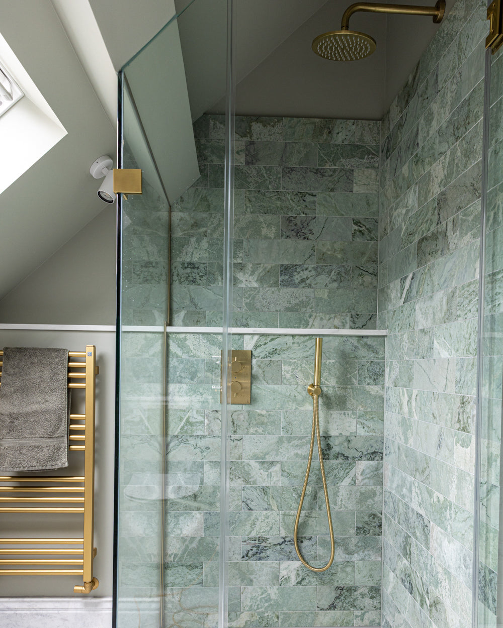 East Java Hummingbird Marble Honed Brick lining a walk-in shower under a sloped ceiling, with a brass rainfall head, brass valve and a heated towel rail alongside