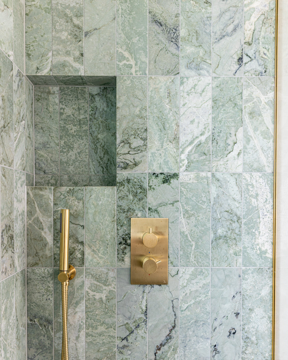 Close detail of East Java Hummingbird Marble Honed Brick around a recessed shower niche, with a brushed brass thermostatic valve and hand shower