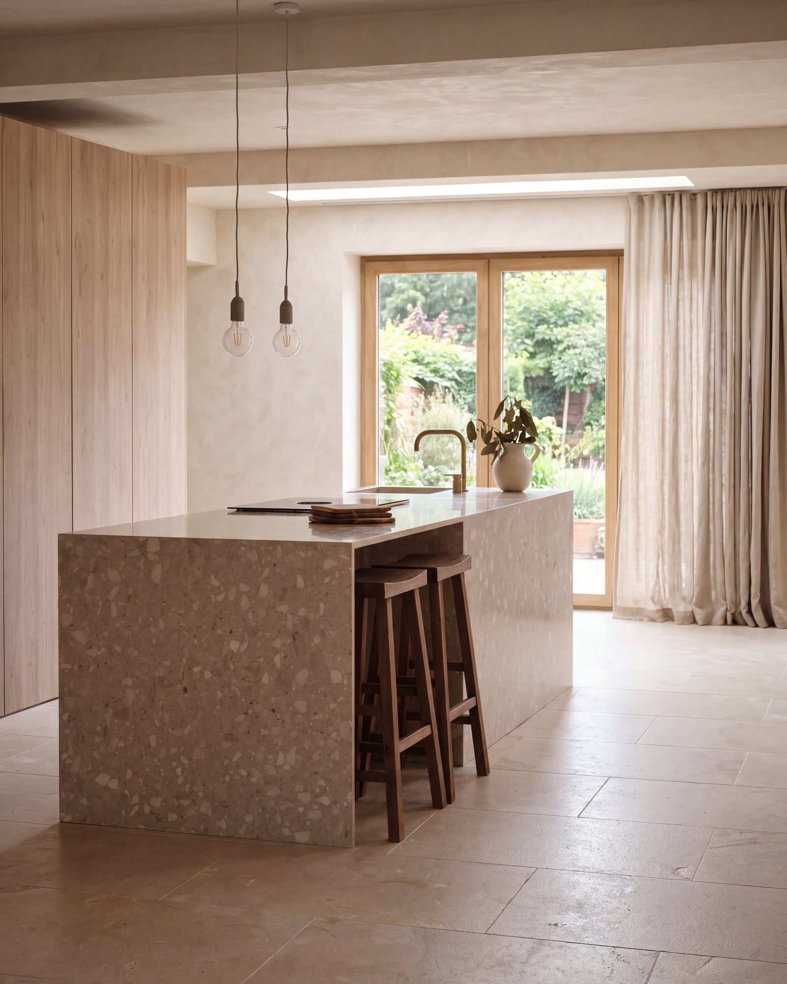 Enki Limestone Velvet Finish running the length of a plaster and pale oak kitchen, past a terrazzo island with walnut bar stools to garden doors