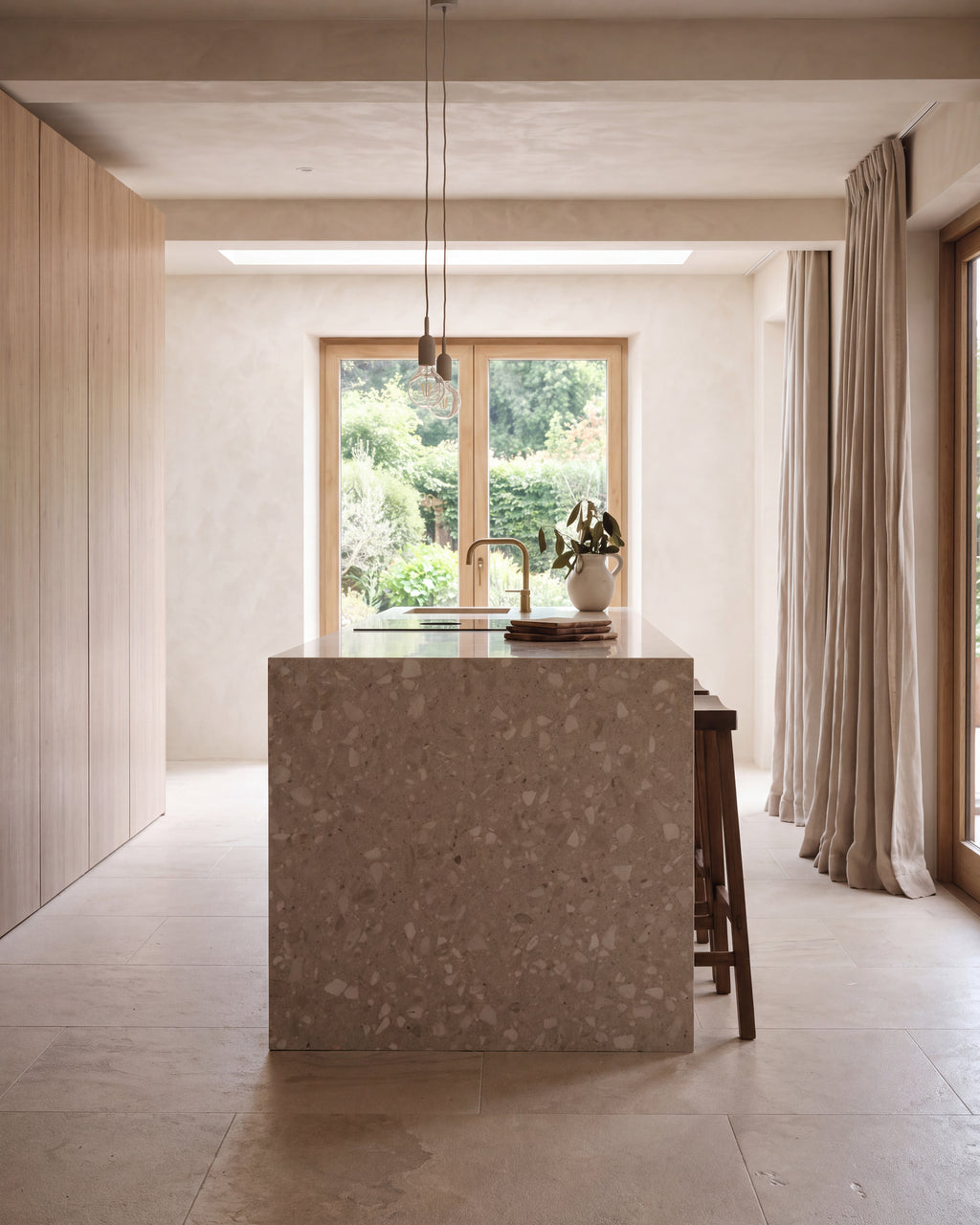 Enki Limestone Velvet Finish in large format around a waterfall terrazzo kitchen island, lit by a rooflight and a garden window with a brass tap