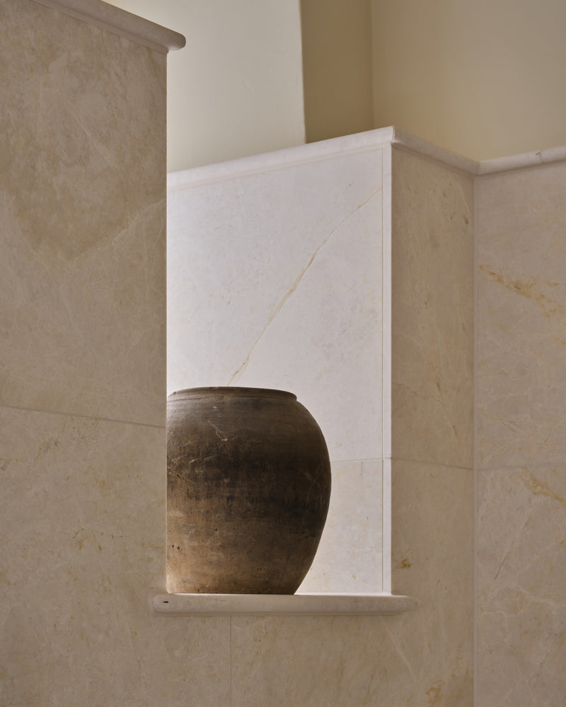 Folio Marble Honed Finish lining a bathroom niche with a bullnose stone shelf holding an antique terracotta pot