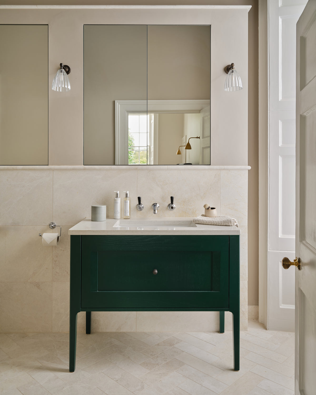 Folio Marble Honed Finish herringbone floor and wall tiling in a bathroom with a dark green vanity and mirrored cabinets