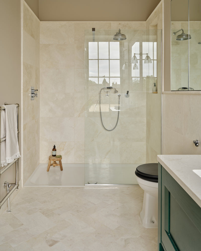 Folio Marble Honed Finish herringbone floor and stone-lined walk-in shower alongside a green painted vanity