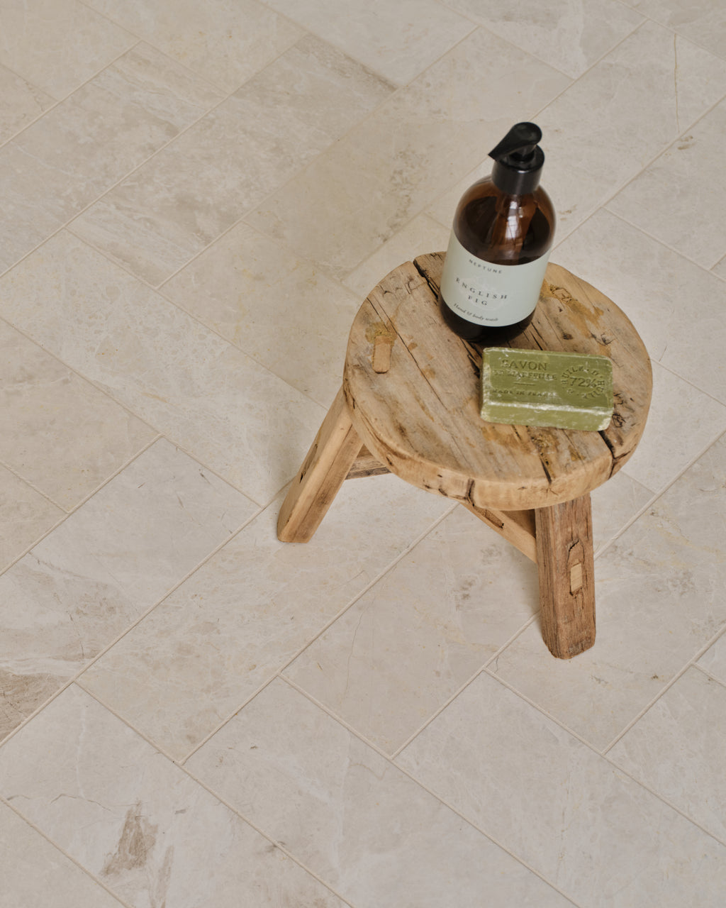 Folio Marble Honed Finish laid in a herringbone pattern with a rustic wooden stool holding hand wash and soap