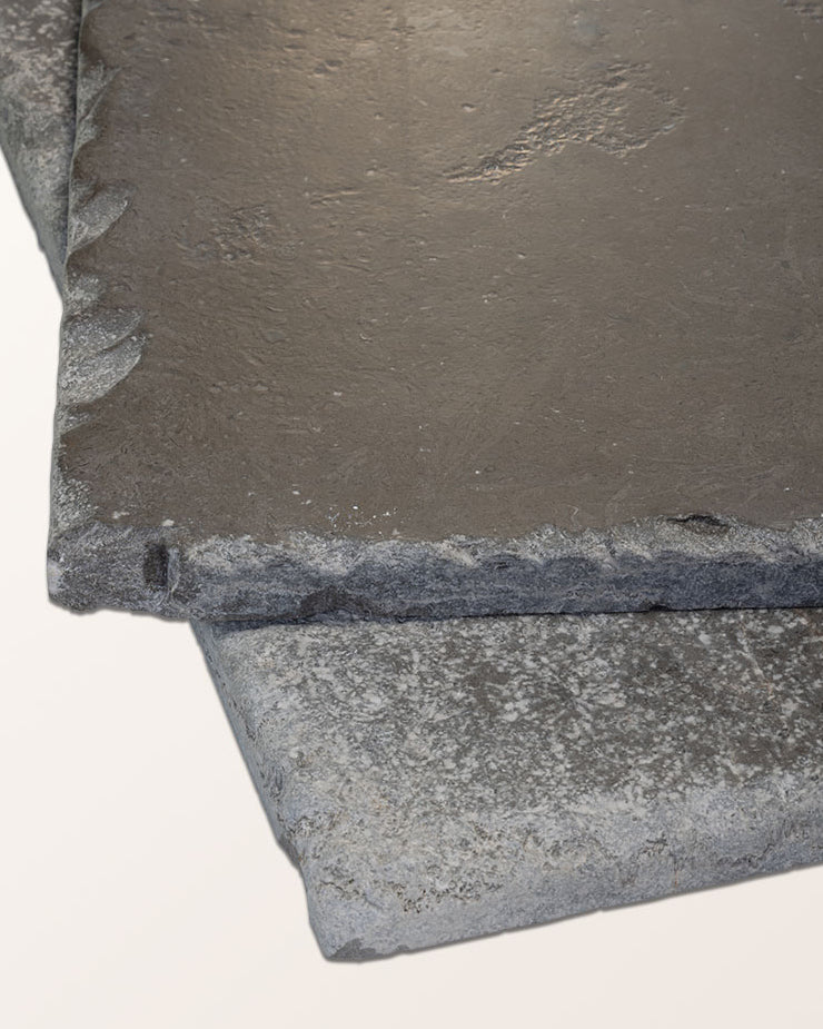 Two Hazlebury Limestone Seasoned Finish tiles stacked to show the tumbled chipped edge profile and honed grey surface