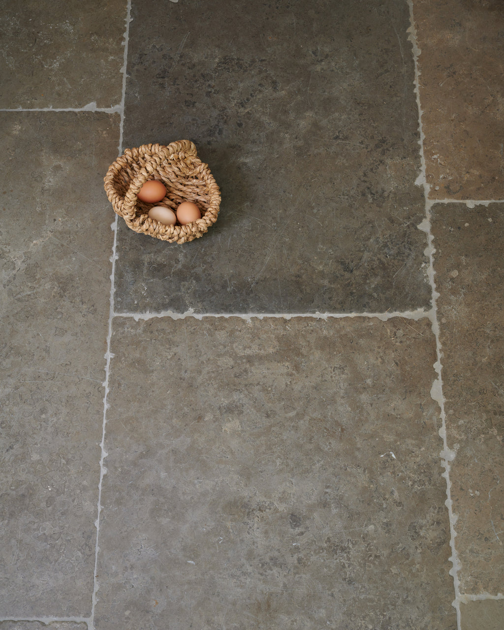 Hazlebury Limestone Seasoned Finish flagstones seen from above, with a woven basket of eggs resting on the mottled grey and ochre surface