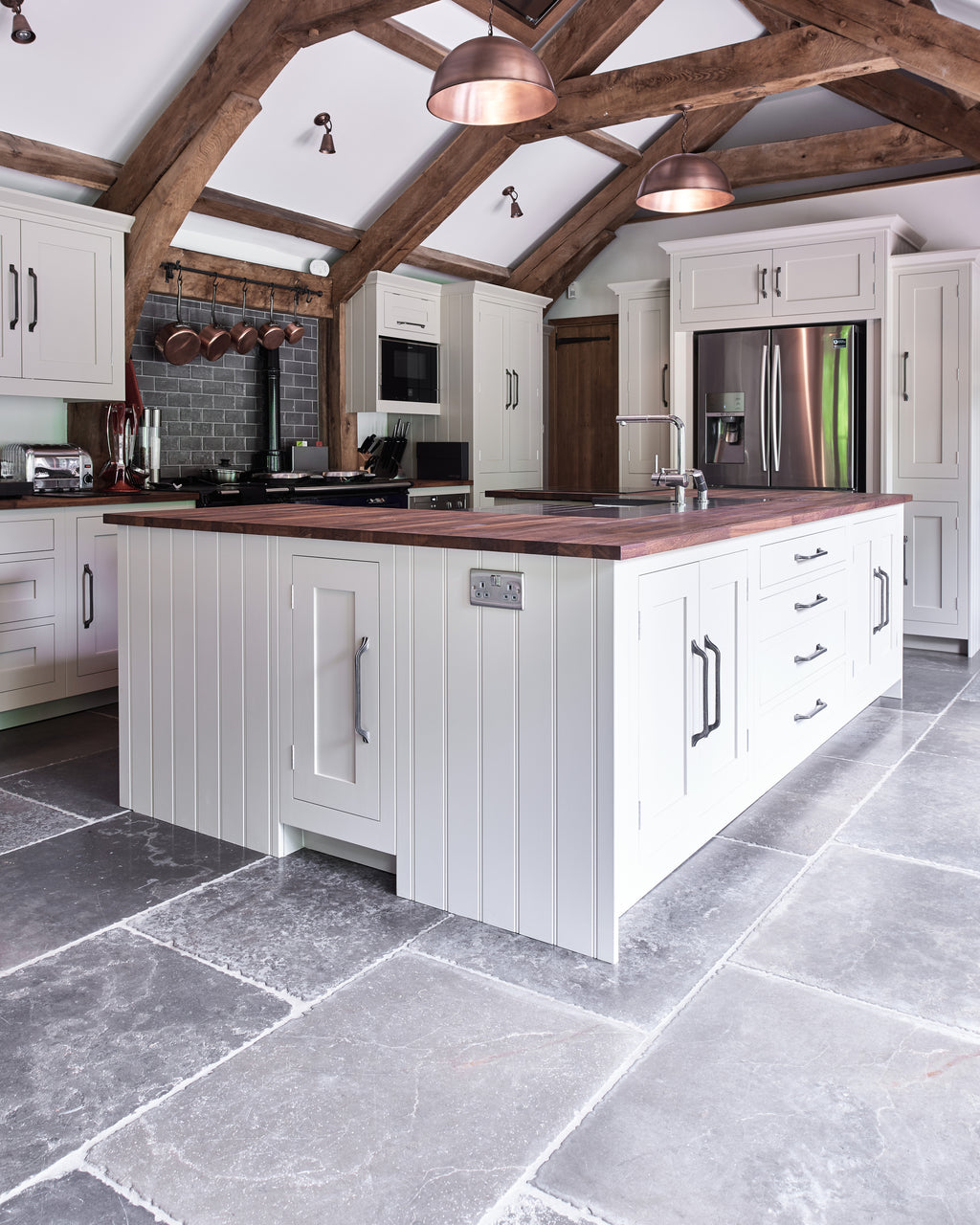Hazlebury Limestone Seasoned Finish flagstones laid across a vaulted barn kitchen with exposed oak trusses, copper pendants and a walnut-topped island