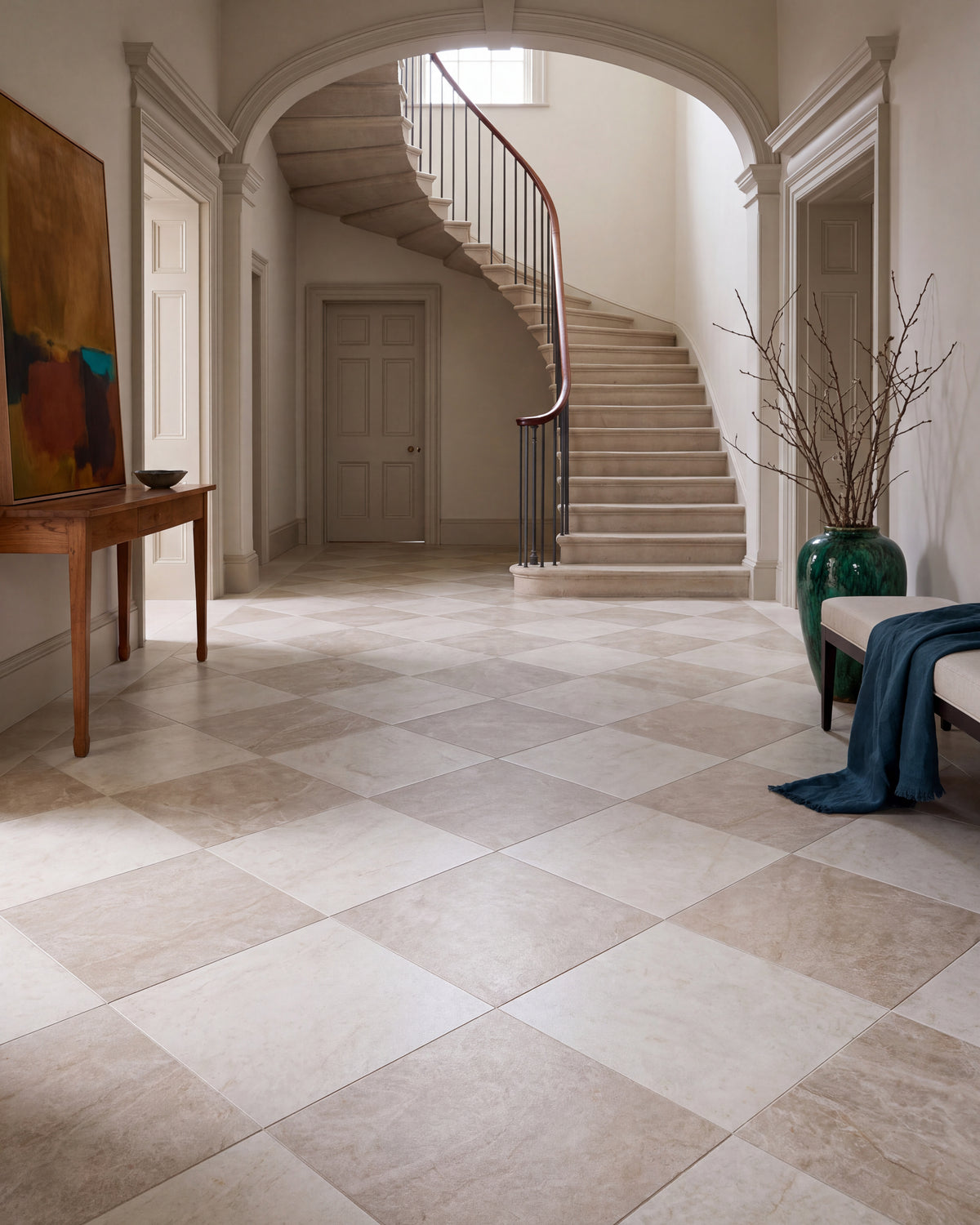 Hoxton Porcelain Amber Matt and Hoxton Porcelain Linen Matt in a diagonal chequerboard across a hallway floor, beneath a stone arch and a curved staircase
