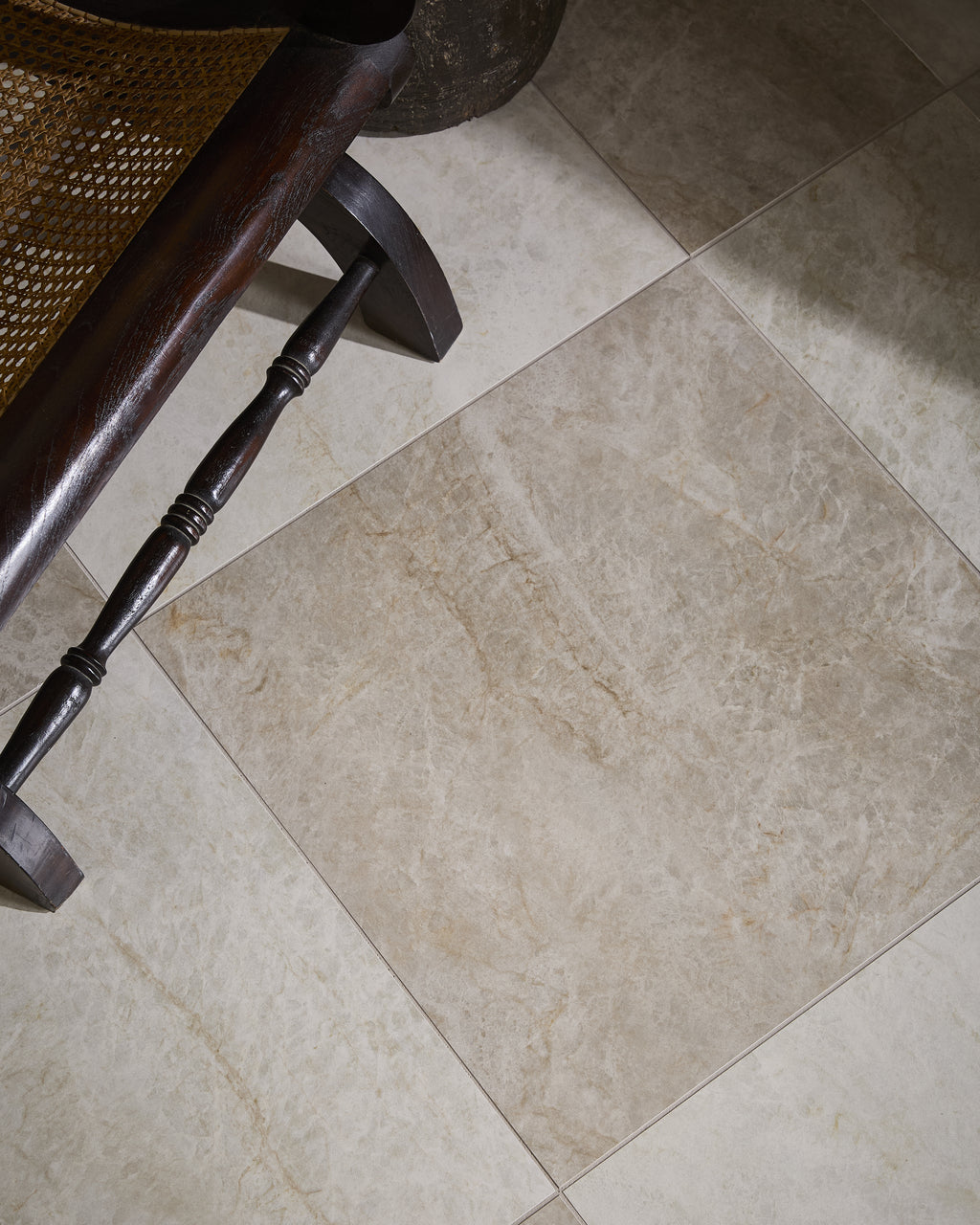 Hoxton Porcelain Linen Matt floor laid diagonally beneath a dark wood and cane plantation chair, with soft daylight falling across the tiles