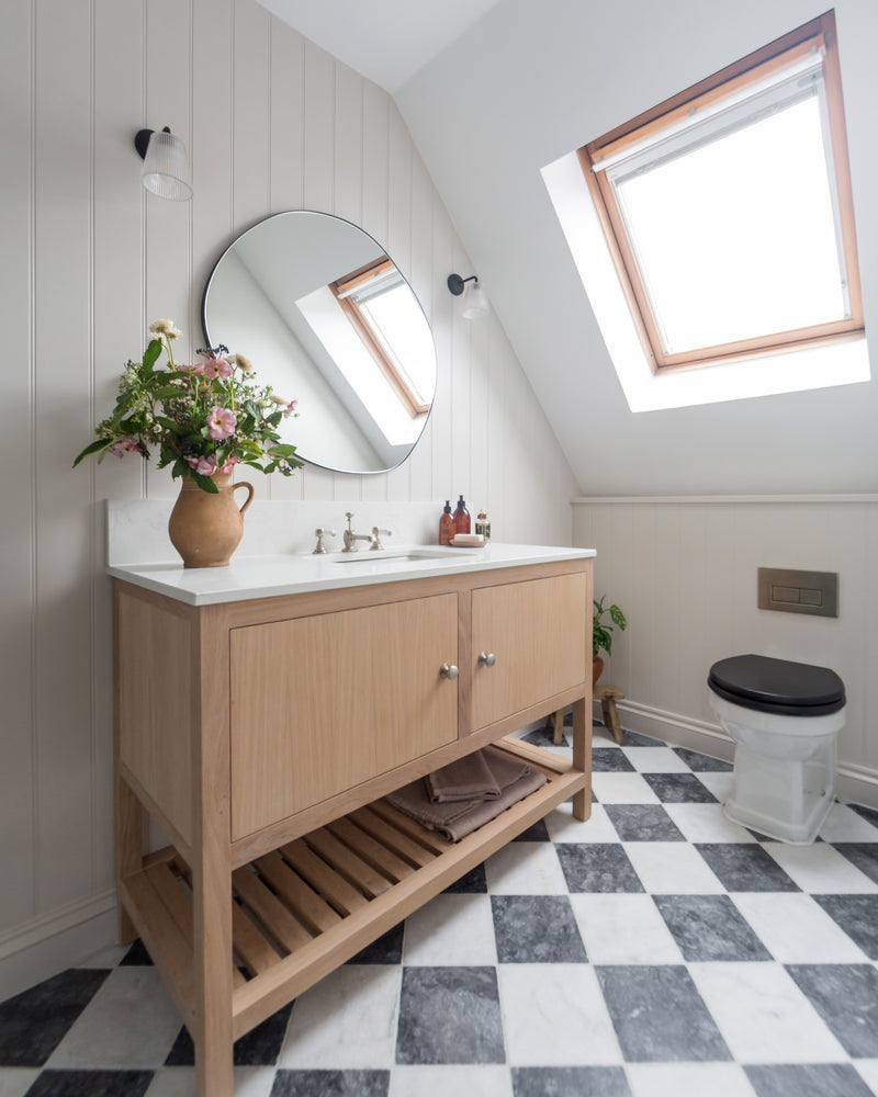 Kendal Marble Tumbled Finish laid as a chequerboard floor with white marble in an attic bathroom, beneath a sloped ceiling and skylight with an oak vanity
