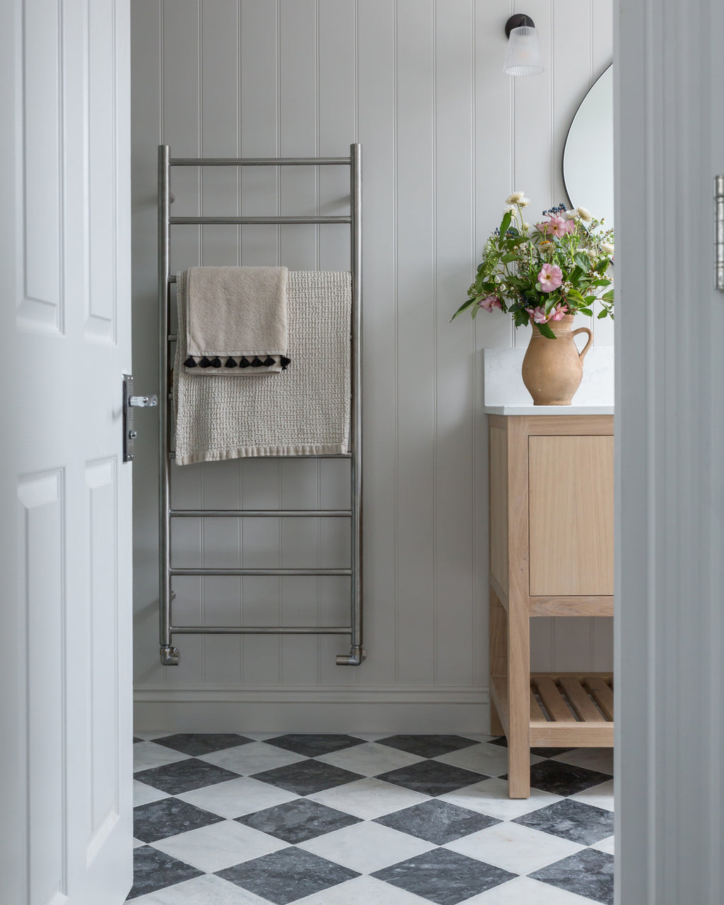 Kendal Marble Tumbled Finish chequerboard floor seen through an open door into a panelled bathroom with a heated towel rail