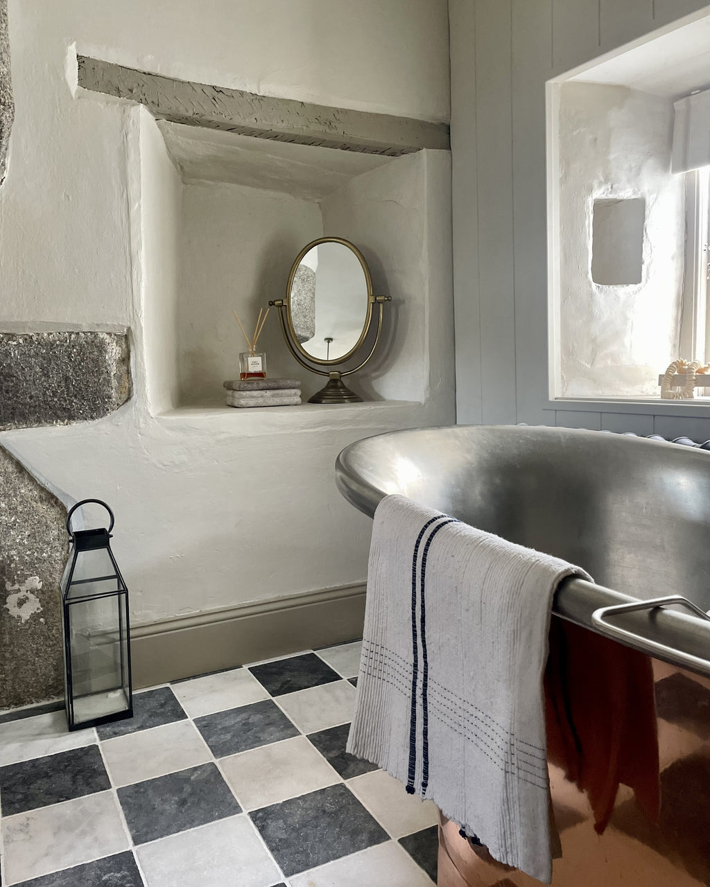 Kendal Marble Tumbled Finish chequerboard floor in a limewashed cottage bathroom with a tin roll top bath and a stone alcove