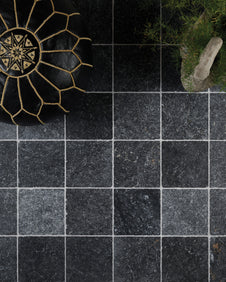 Overhead view of Kendal Marble Tumbled Finish laid square with pale grout, styled with a black and gold Moroccan leather pouffe and an asparagus fern