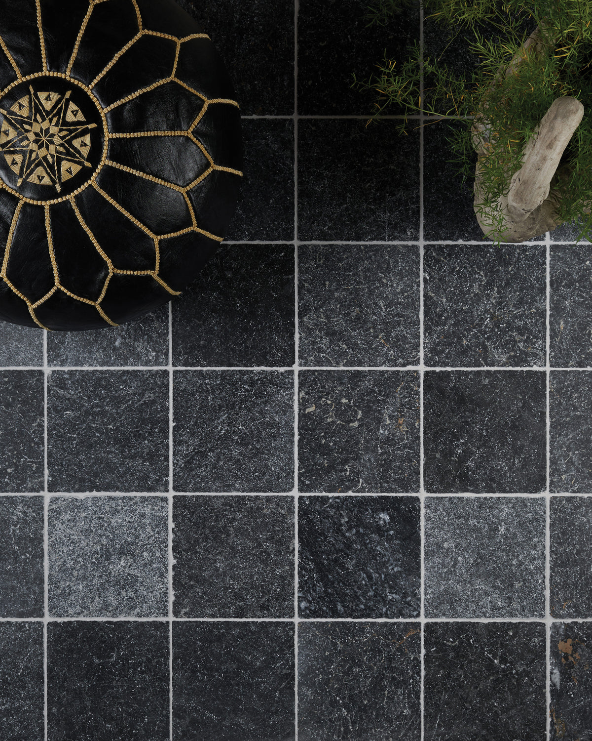 Overhead view of Kendal Marble Tumbled Finish laid square with pale grout, styled with a black and gold Moroccan leather pouffe and an asparagus fern