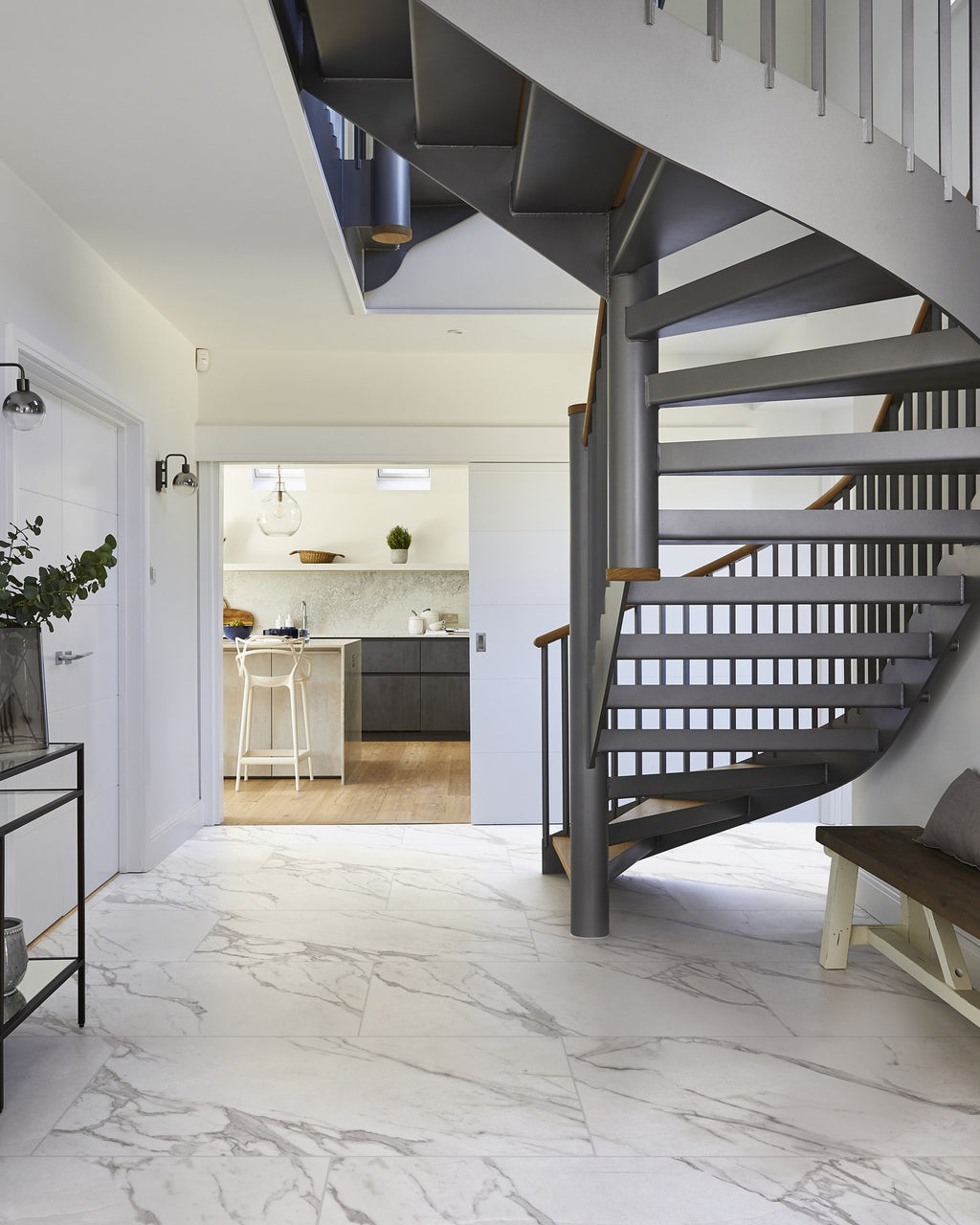 Kensington Porcelain Matt laid across a large hallway floor beneath a grey spiral staircase, looking through to the kitchen