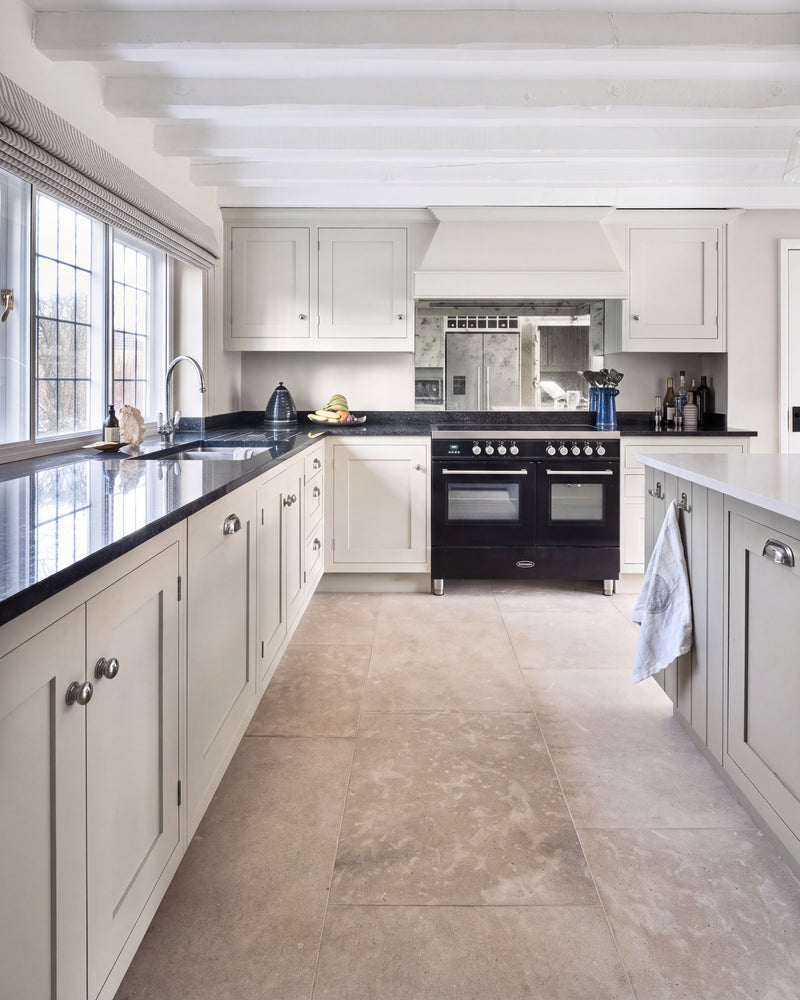 Kimmeridge Limestone Etched Finish in large format across a beamed country kitchen floor, running between pale shaker cabinets with black granite worktops and a black range cooker