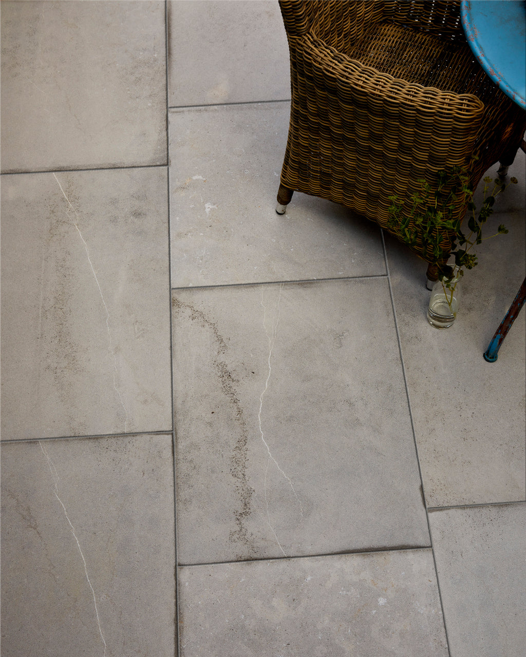 Kimmeridge Limestone Etched Finish laid in a staggered bond on a terrace, seen close up beneath a wicker chair and a weathered blue bistro table
