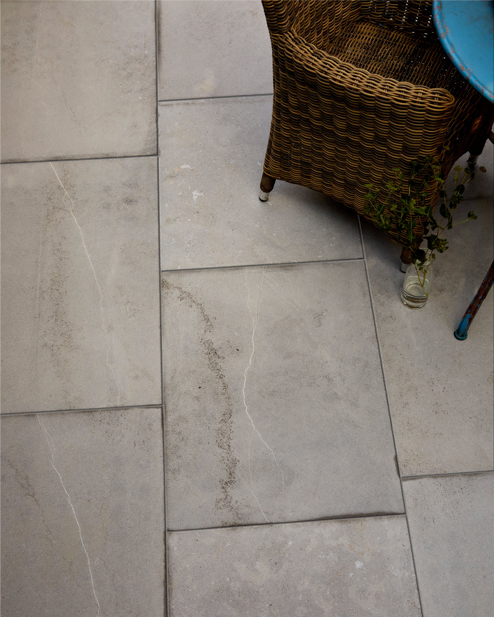 Kimmeridge Limestone Etched Finish laid in a staggered bond on a terrace, seen close up beneath a wicker chair and a weathered blue bistro table