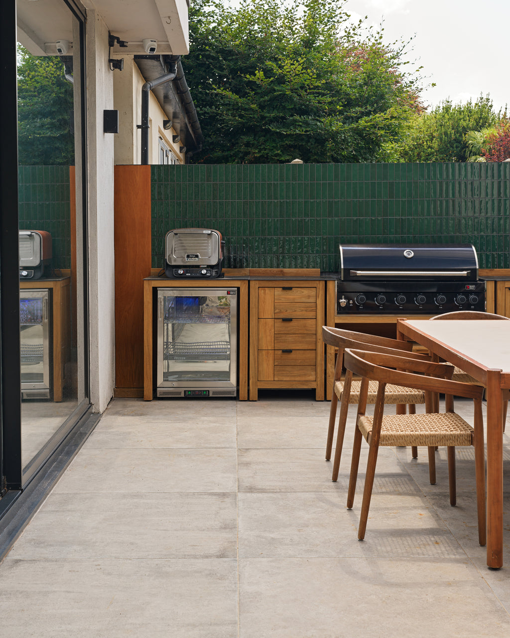 Kimmeridge Limestone Paving Etched Finish underfoot in an outdoor kitchen, with a teak grill run set against a Petite Green Gloss tiled wall
