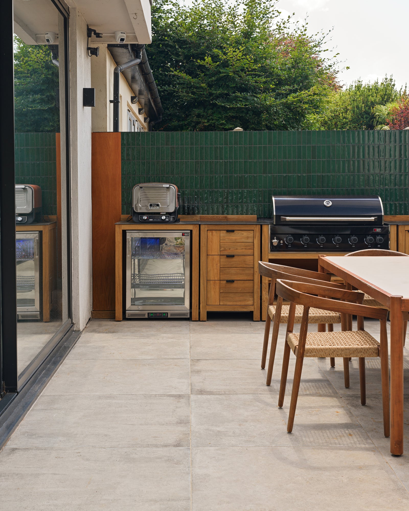 Kimmeridge Limestone Paving Etched Finish underfoot in an outdoor kitchen, with a teak grill run set against a Petite Green Gloss tiled wall