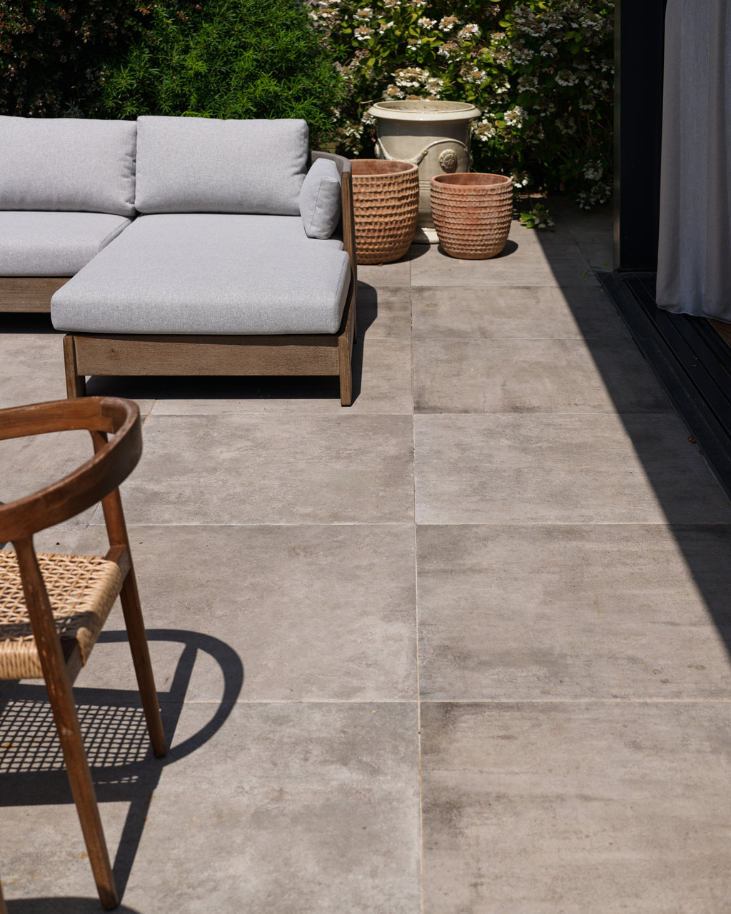 Kimmeridge Limestone Paving Etched Finish in large format across a sunlit terrace, with a grey outdoor sofa and terracotta pots against a flowering hedge