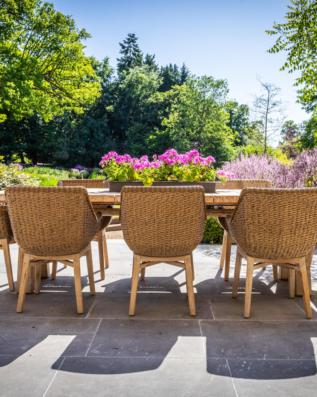Kimmeridge Limestone Paving Tumbled & Etched Finish laid across a sunlit garden terrace with a long oak table and woven wicker dining chairs