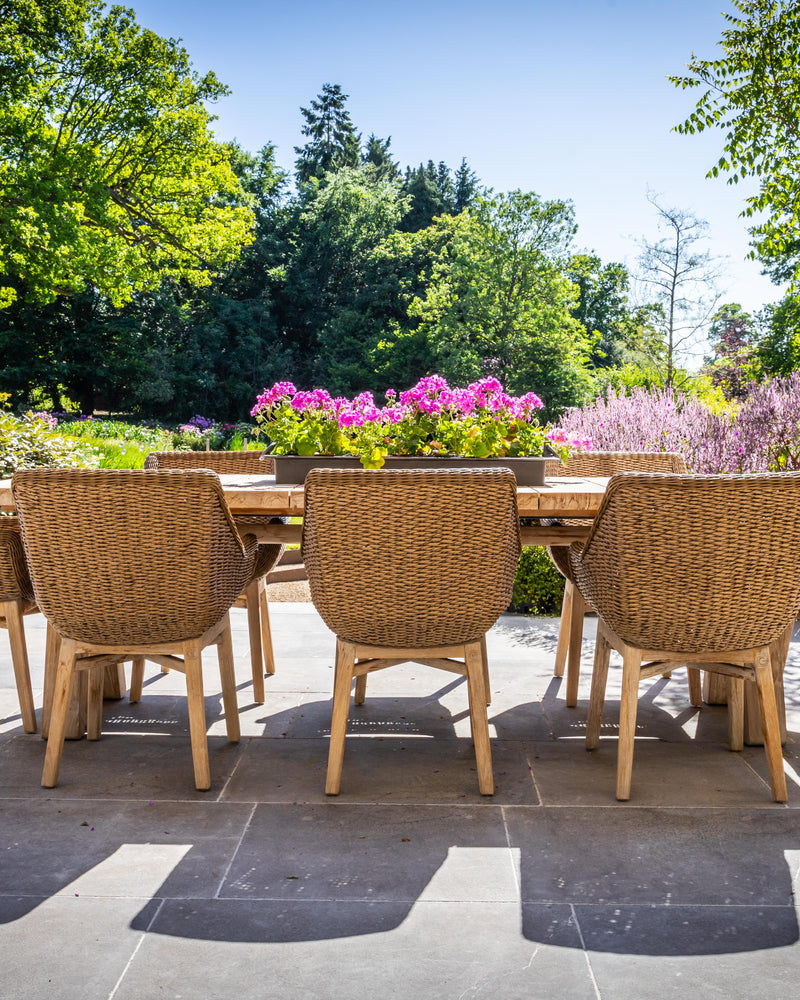 Kimmeridge Limestone Paving Tumbled & Etched Finish laid across a sunlit garden terrace with a long oak table and woven wicker dining chairs