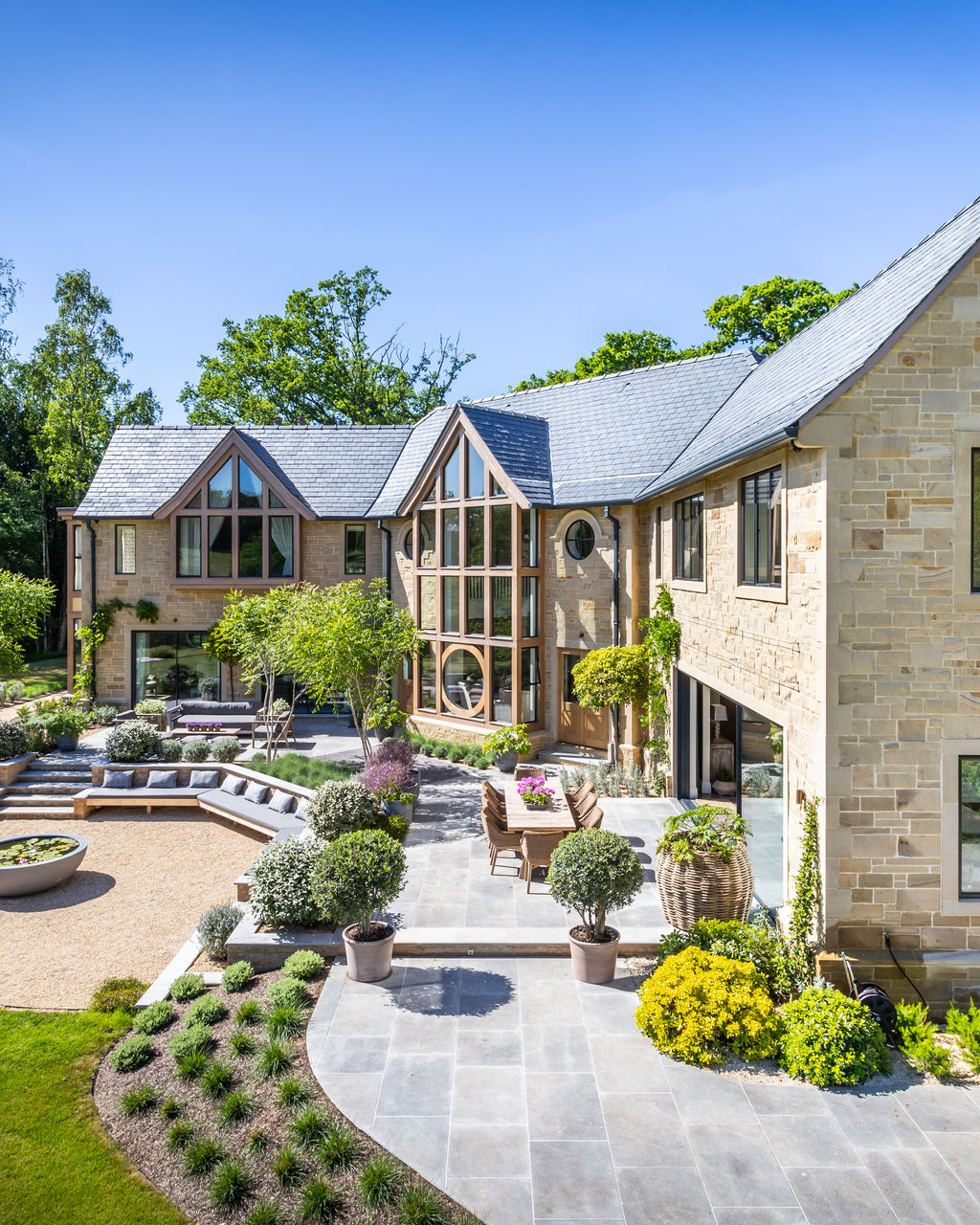 Kimmeridge Limestone Paving Tumbled & Etched Finish sweeping through a landscaped garden of a stone house, linking a gravel courtyard to the terrace and steps