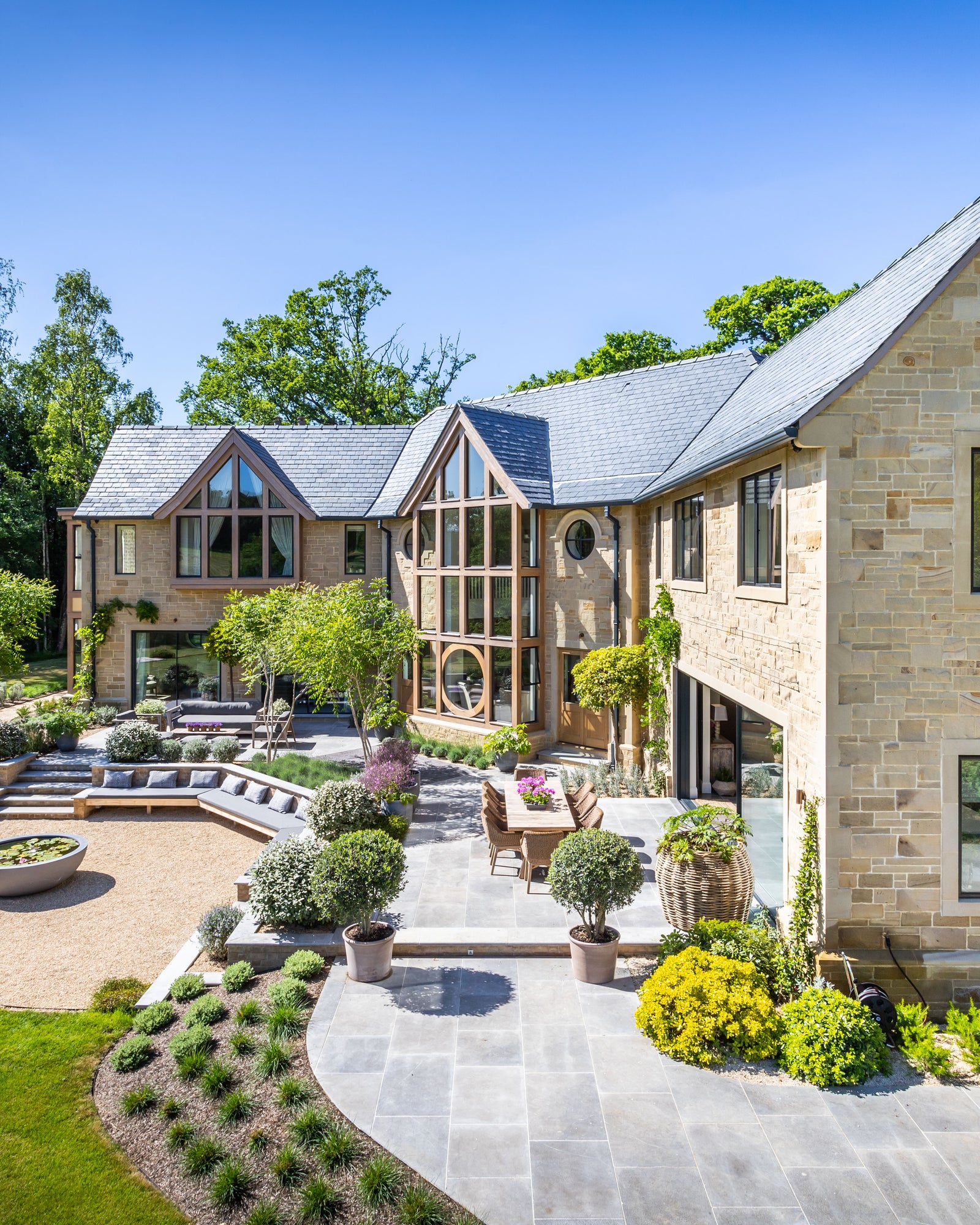 Kimmeridge Limestone Paving Tumbled & Etched Finish sweeping through a landscaped garden of a stone house, linking a gravel courtyard to the terrace and steps