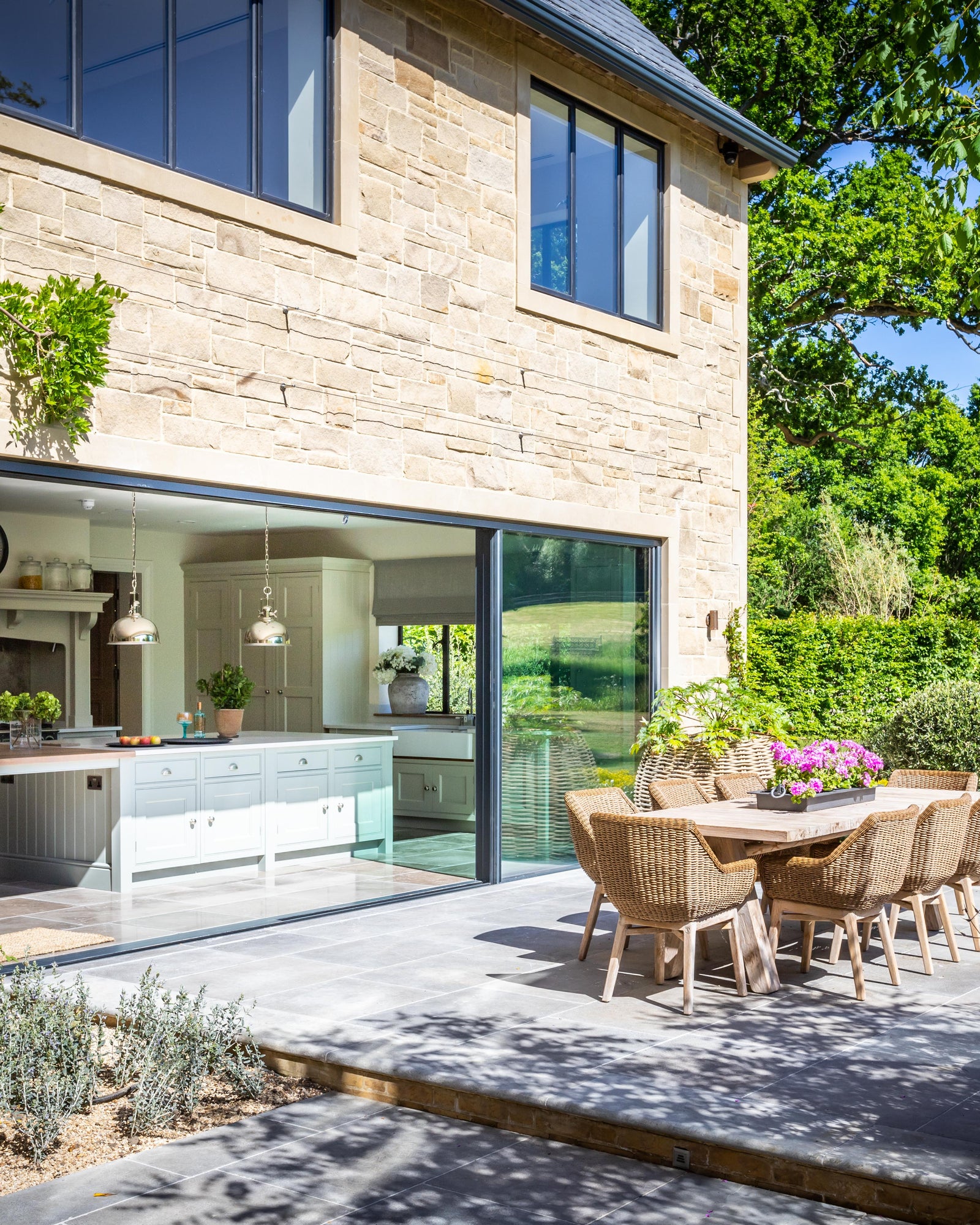 Kimmeridge Limestone Paving Tumbled & Etched Finish on a dining terrace outside open sliding doors onto a pale green country kitchen