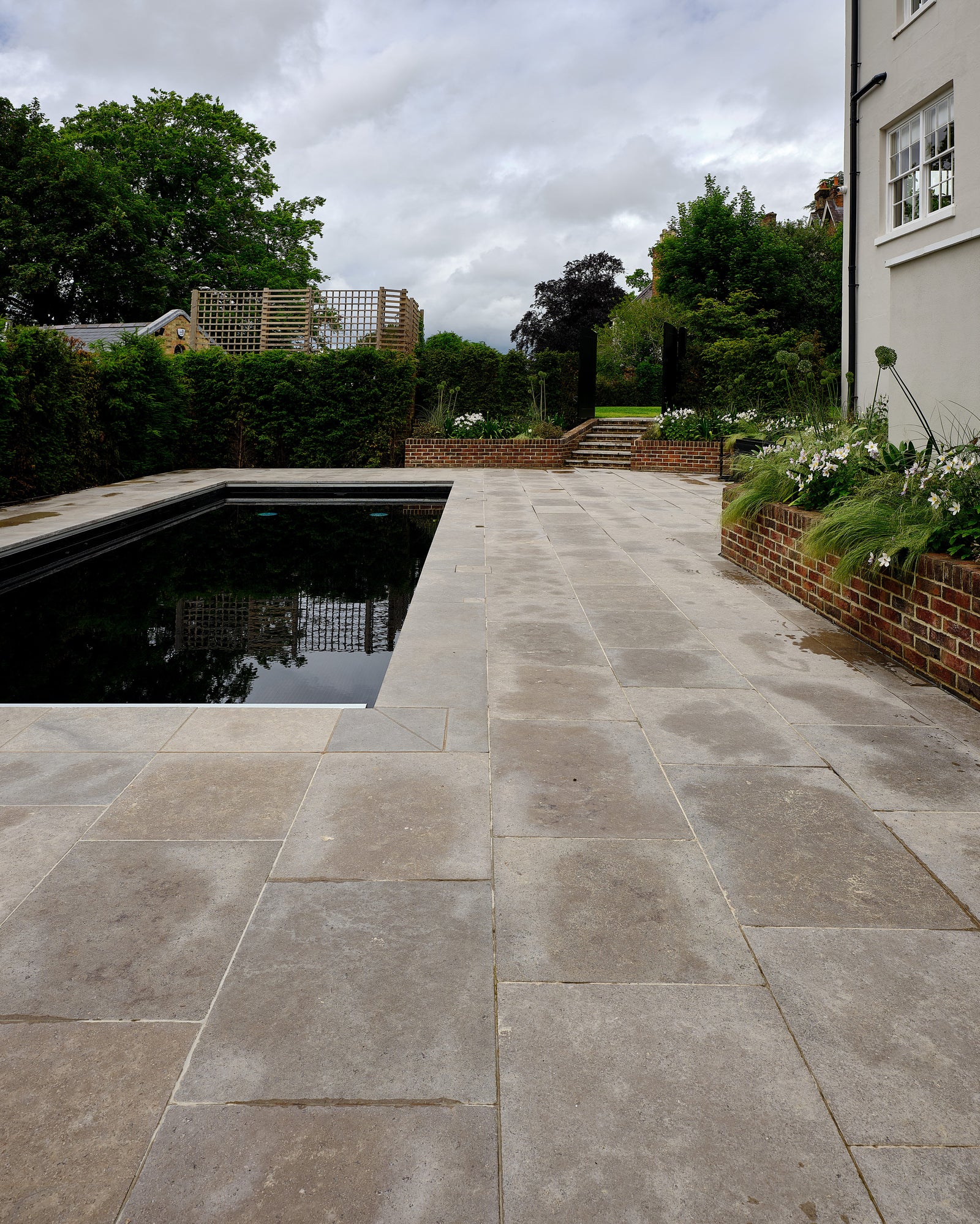 Kimmeridge Limestone Tumbled & Etched Finish laid around a dark rectangular swimming pool beside a white rendered house, damp from rain