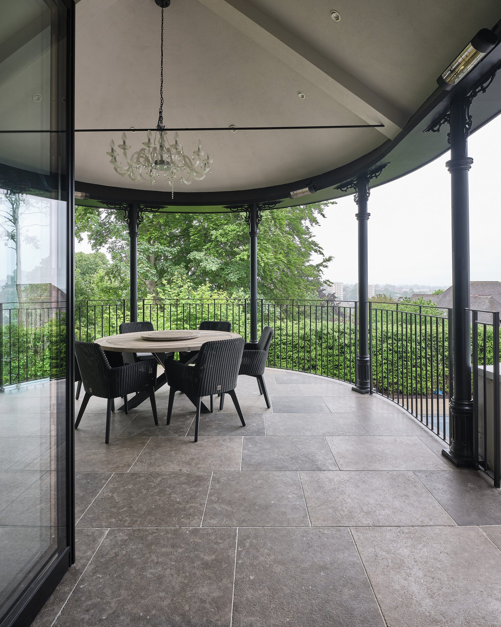 Kimmeridge Limestone Tumbled & Etched Finish across a curved covered veranda with cast iron columns, a round dining table and a glass chandelier