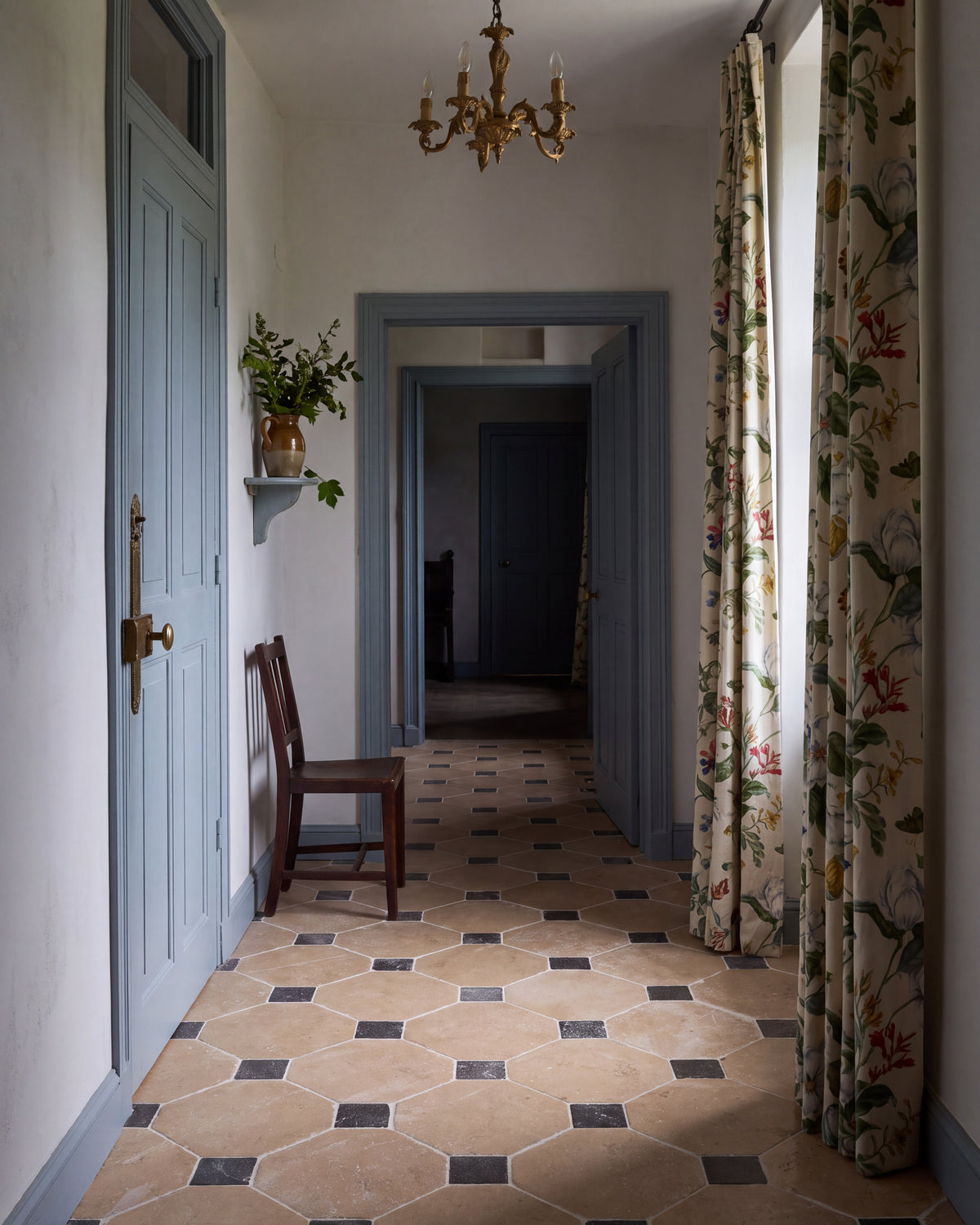 Lacock Limestone Heritage Finish Octagons with Hazlebury Cabochons running the length of a hallway with blue-grey painted doors, floral curtains, a wooden chair and a gilt chandelier