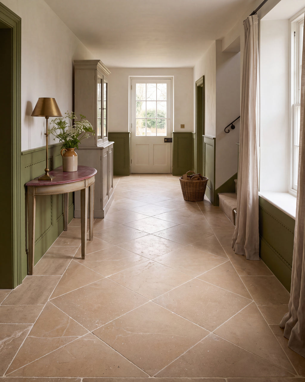 Lacock Limestone Tumbled Finish in 60x60cm laid on the diagonal down a long country hallway with olive green panelling, a demi-lune console and a glazed garden door