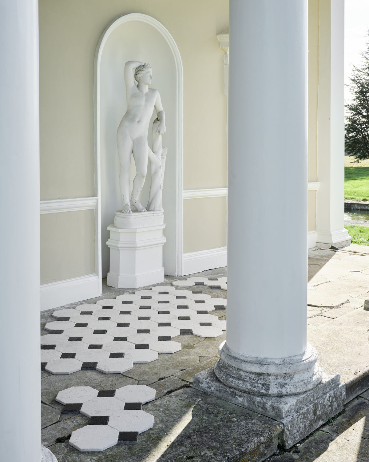 Limoges Limestone Vintaged Finish octagons with Tora Blue Limestone Vintaged Cabochons laid out on the flagstone floor of a classical garden portico beside a marble statue