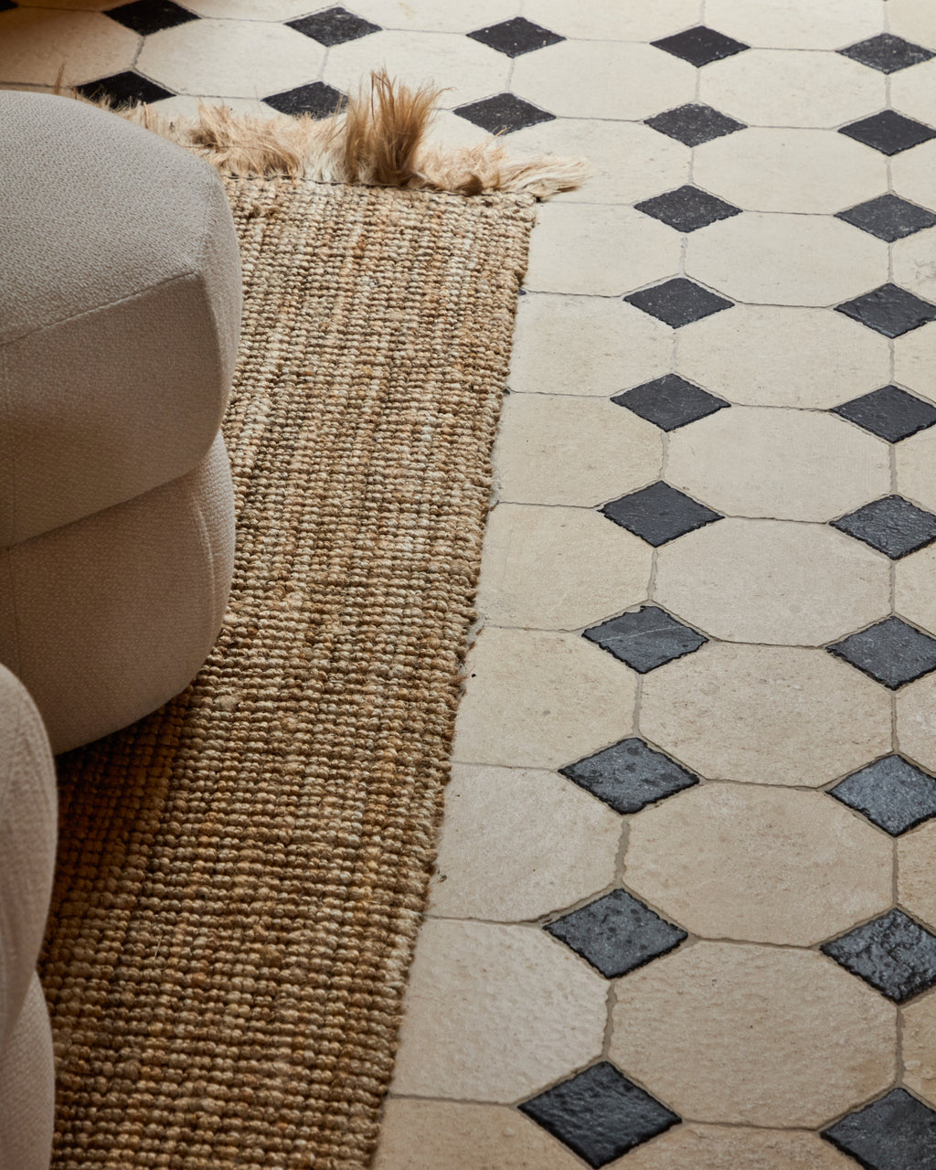 Detail of a Limoges Limestone Vintaged Finish octagon floor with Tora Blue cabochons running alongside a jute rug