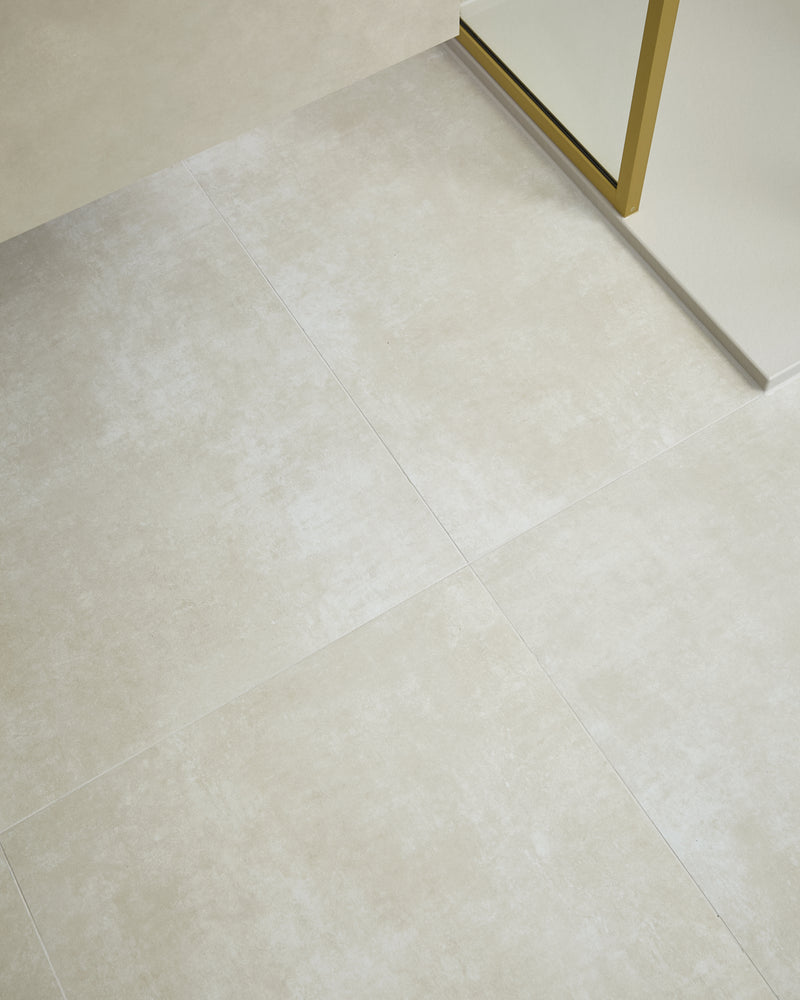 Loft Porcelain Pearl laid large format across a bathroom floor and up the wall, meeting a brushed brass shower screen frame