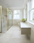 Loft Porcelain Pearl on the floor and walls of a long bathroom with a brass framed walk-in shower, floating vanity and arched mirror