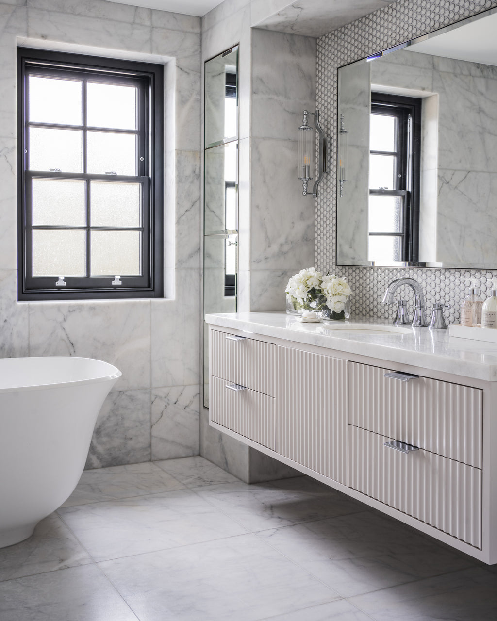 Long Island Marble Honed Finish in large format across the walls and floor of a bathroom with a freestanding bath, fluted vanity and black sash window