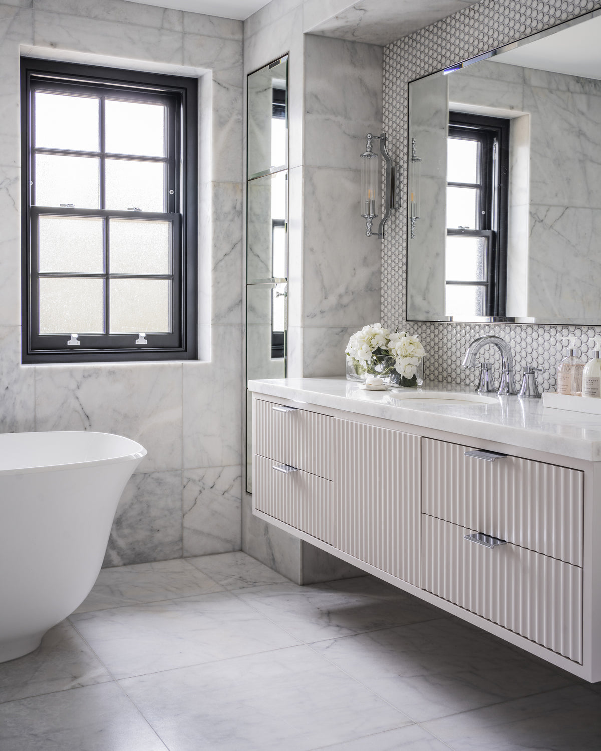 Long Island Marble Honed Finish in large format across the walls and floor of a bathroom with a freestanding bath, fluted vanity and black sash window