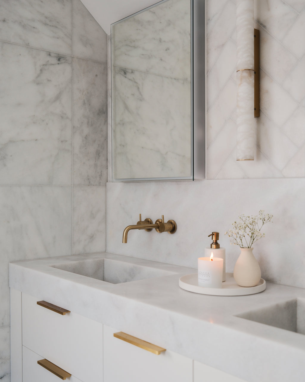 Long Island Marble Honed Slab worked into a vanity top with an integral trough basin, set against honed marble walls with brass wall-mounted taps and an alabaster wall light