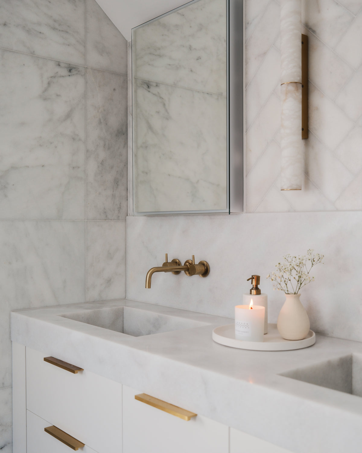 Long Island Marble Honed Slab worked into a vanity top with an integral trough basin, set against honed marble walls with brass wall-mounted taps and an alabaster wall light