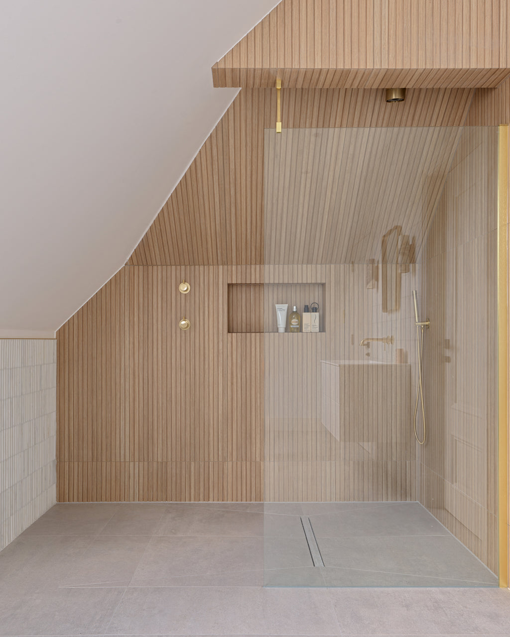 Louvre Porcelain Perla fluted tile in a loft bathroom, running as a dado beside a walk-in shower lined in warm timber-effect fluting with brushed brass fittings and a recessed niche